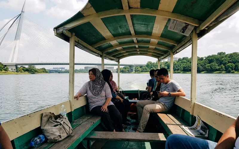 A covered traditional perahu crossing the Putrajaya lake under a clear bright sky