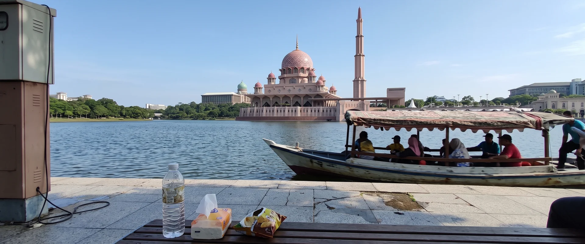 The Putra Mosque pink dome across the Putrajaya lake with a traditional covered perahu passing