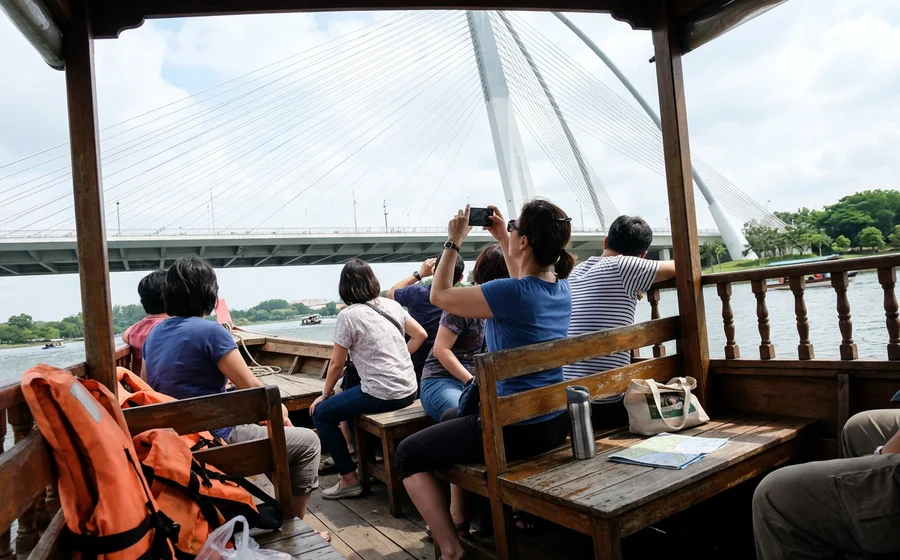 Passengers seated inside a covered traditional perahu on the Putrajaya lake looking out at Seri Wawasan bridge