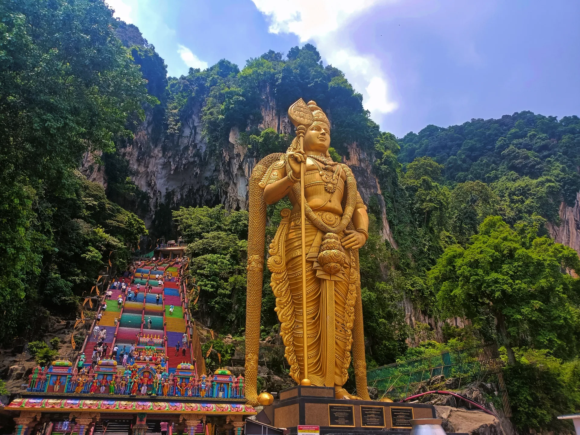 The Lord Murugan statue and the rainbow staircase at Batu Caves, with visitors on the steps